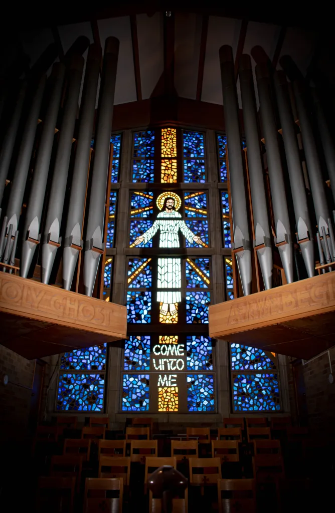 Stained glass window depicting Jesus framed by organ pipes, radiating divine light and serenity.